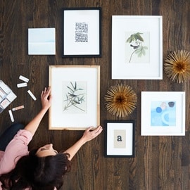 Woman making a mockup of her gallery wall before hanging on the wall. Command Picture Hanging Strips on display as well.