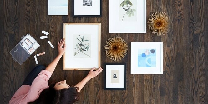 Woman making a mockup of her gallery wall before hanging on the wall. Command Picture Hanging Strips on display as well.
