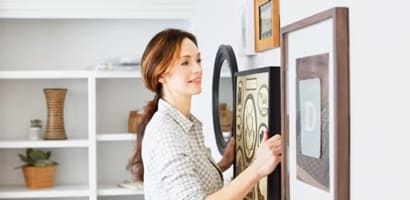 A woman hanging a picture using decorative picture hanger hooks
