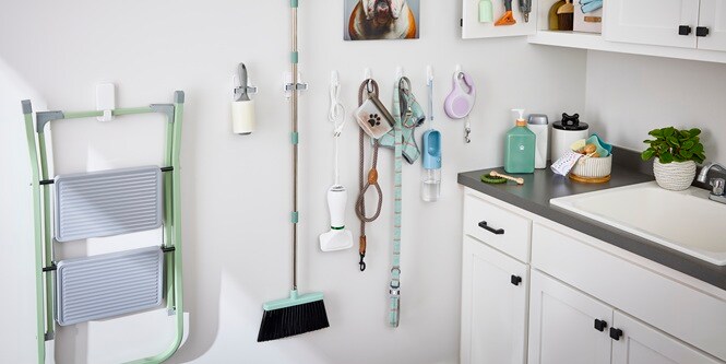 Leashes, dog accessories, mop holder and cleaning tools all hanging on white Command™ hooks along a wall
