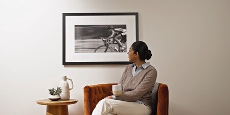 A woman seated on a couch, looking at artwork mounted with Command picture hanging strips.
